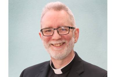 Head and shoulders of man smiling to camera, wearing a clerical collar and black shirt
